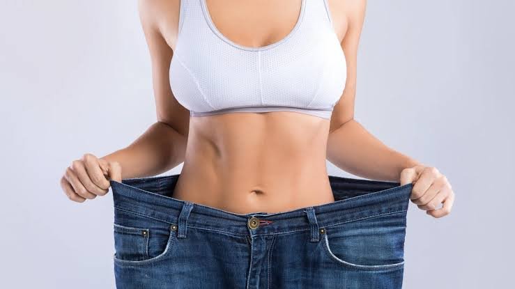 Mulher segurando uma calça jeans larga na cintura, representando o emagrecimento