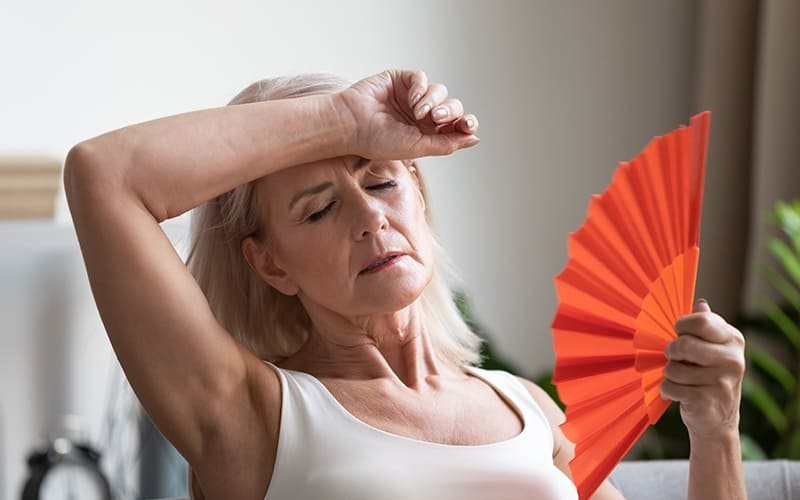 Mulher se abanando com um leque durante um calor, representando os sintomas da menopausa