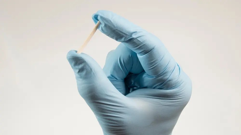 Mão de luvas segurando um pellet, representando a reposição hormonal com acompanhamento médico